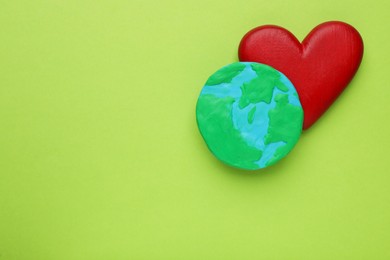 Photo of Model of planet and red heart on green background, flat lay with space for text. Earth Day