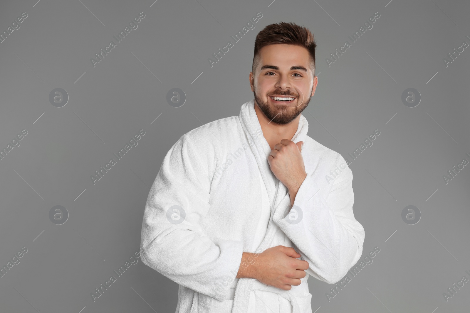 Photo of Happy young man in bathrobe on grey background