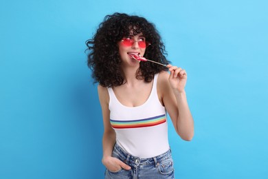 Beautiful woman in sunglasses with lollipop on light blue background