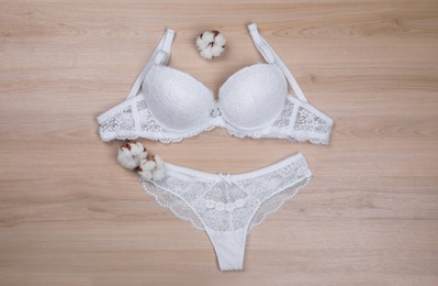Elegant white women's underwear and cotton flowers on wooden background, flat lay