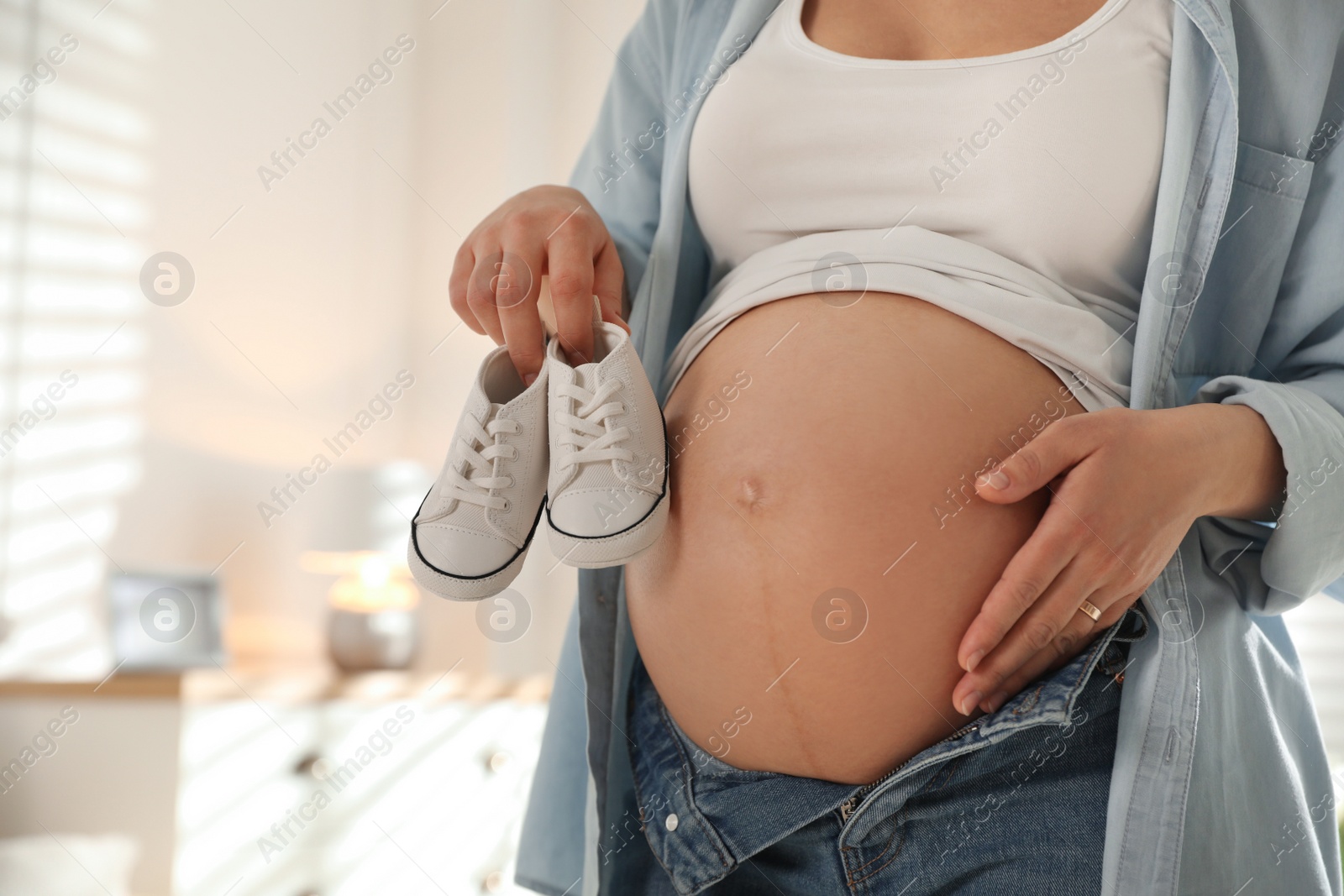 Photo of Young pregnant woman with baby's shoes indoors, closeup. Space for text