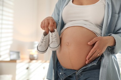 Photo of Young pregnant woman with baby's shoes indoors, closeup. Space for text