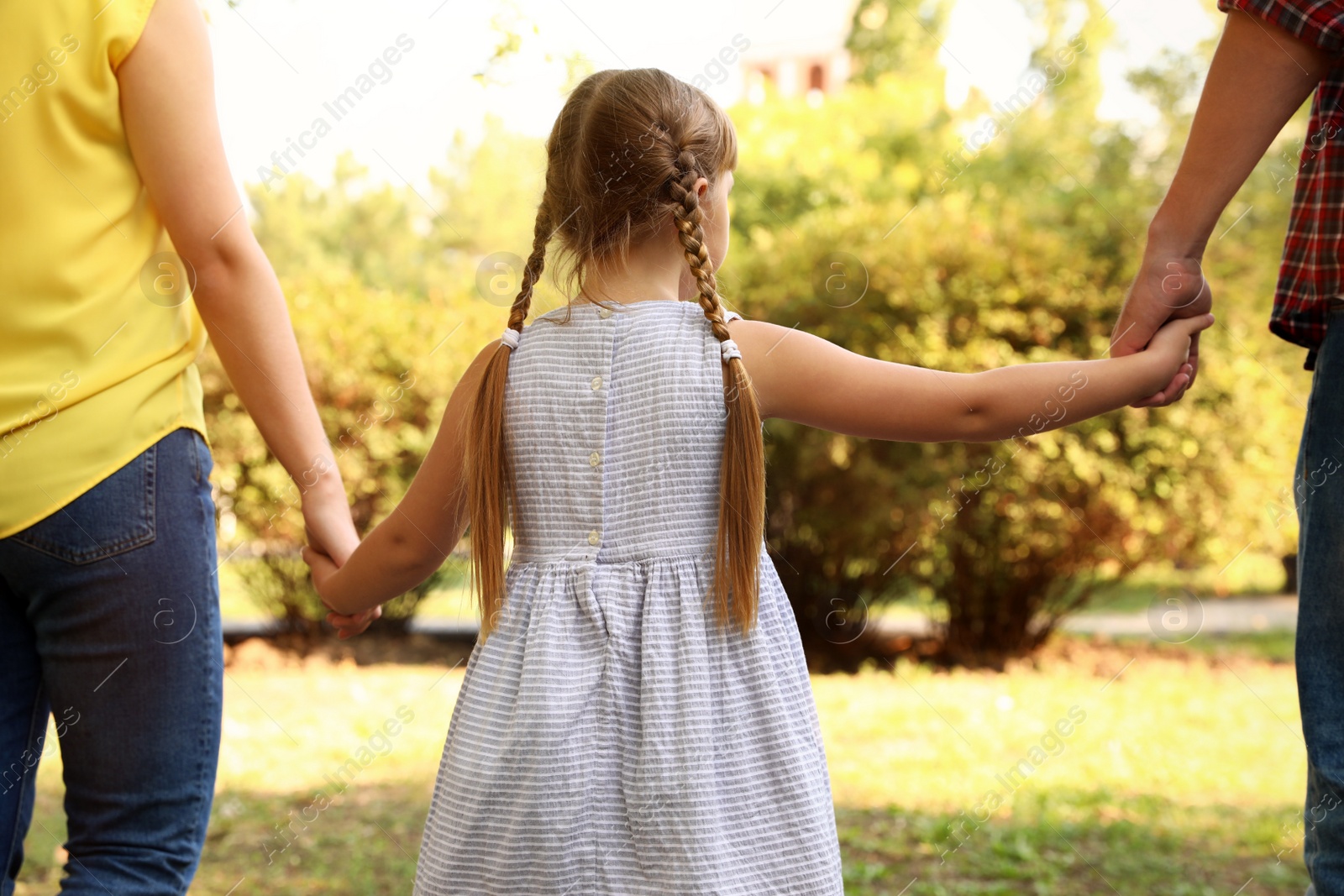 Photo of Little girl and her parents holding hands outdoors. Family weekend