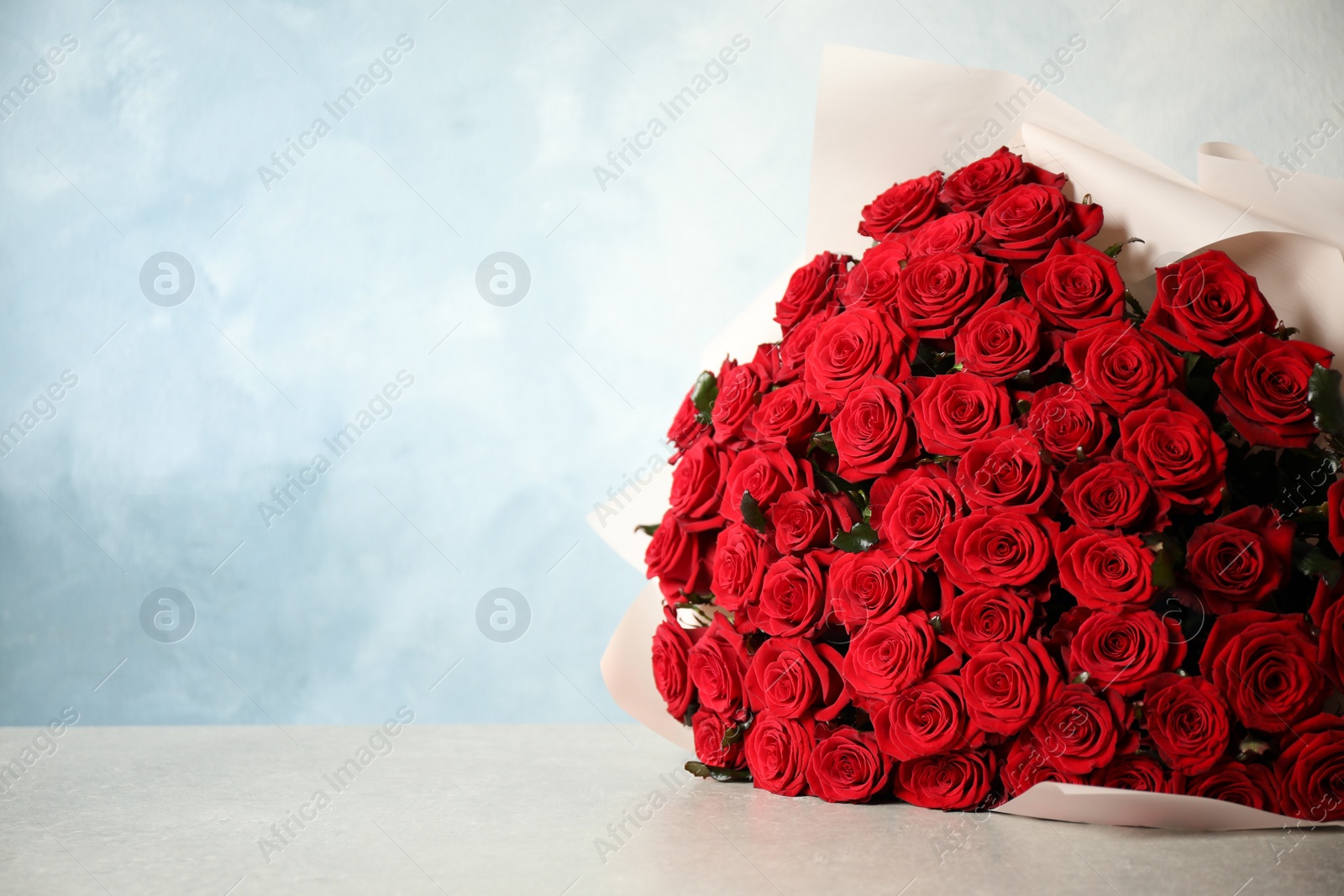 Photo of Luxury bouquet of fresh red roses on light table, space for text