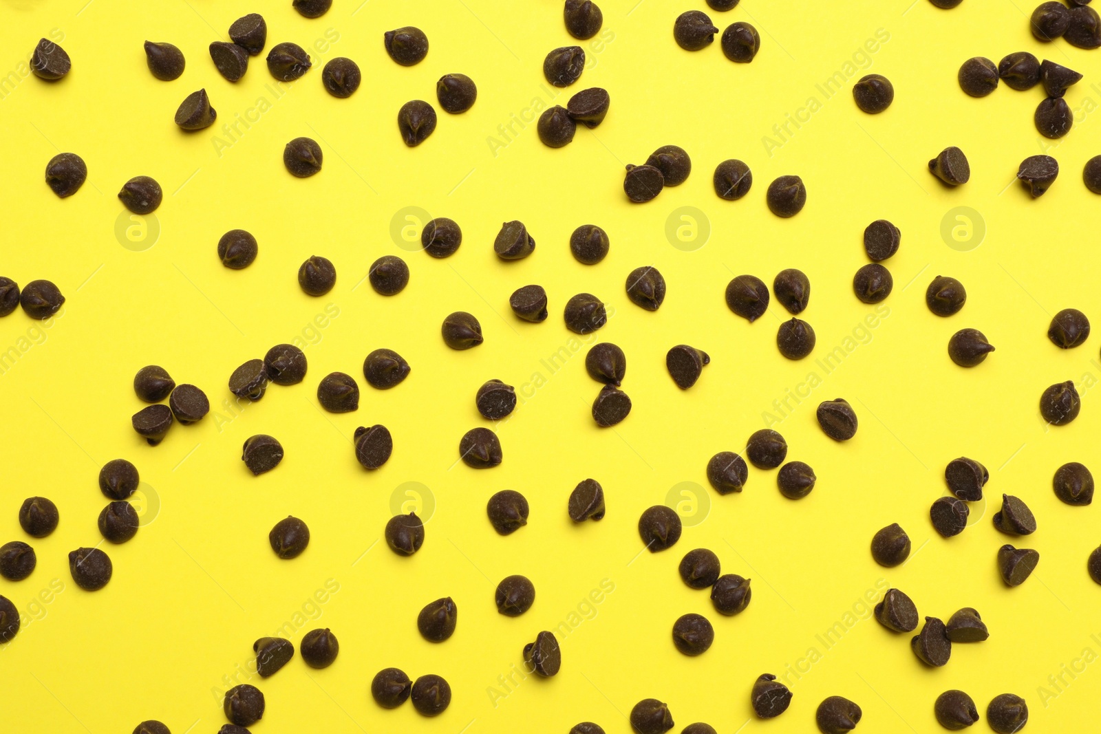 Photo of Delicious chocolate chips on yellow background, top view