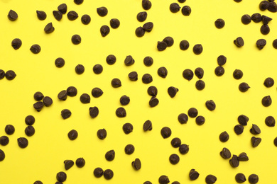 Photo of Delicious chocolate chips on yellow background, top view