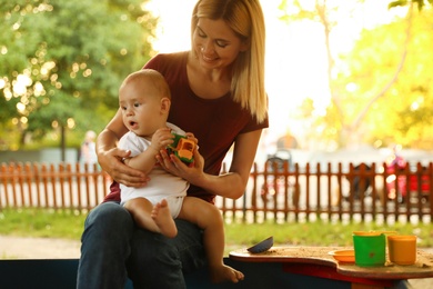 Photo of Nanny and cute little baby playing with toys outdoors