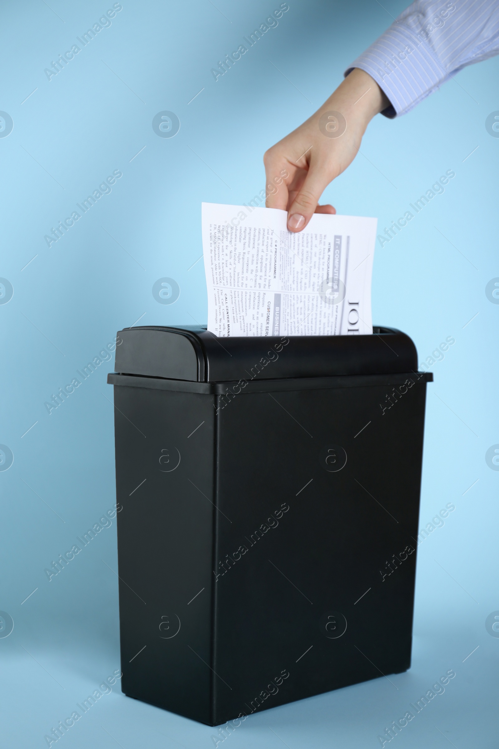 Photo of Woman destroying sheet of paper with shredder on light blue background, closeup