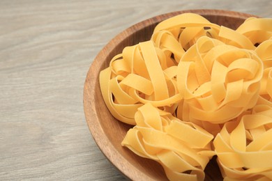 Raw tagliatelle pasta in bowl on light grey wooden table, closeup. Space for text