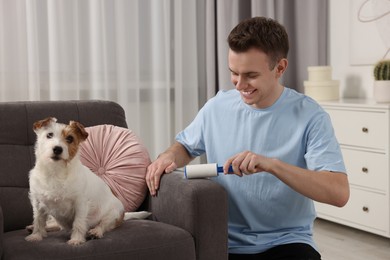 Photo of Smiling man removing pet's hair from armchair at home