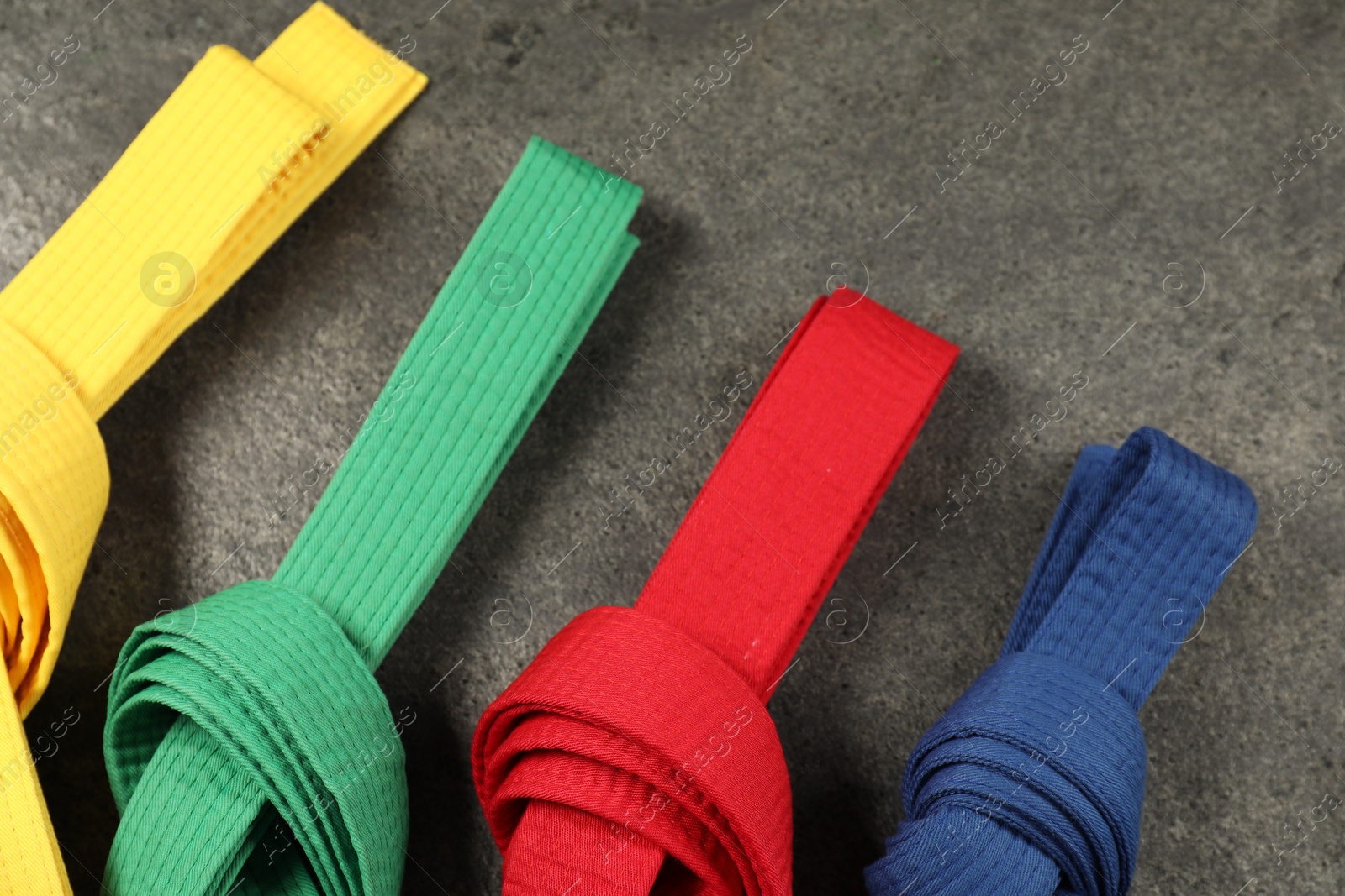 Photo of Colorful karate belts on gray background, flat lay