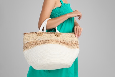 Young woman with stylish straw bag on light grey background, closeup