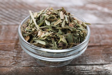 Photo of Glass bowl with aromatic dried lemongrass on wooden table, closeup