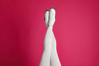 Woman in elegant white ice skates on pink background, closeup of legs