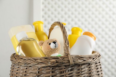 Wicker basket full of different baby cosmetic products and toy on blurred background, closeup