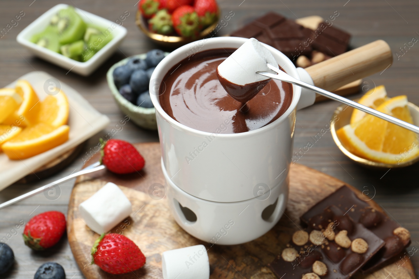 Photo of Dipping sweet marshmallow in fondue pot with melted chocolate at wooden table