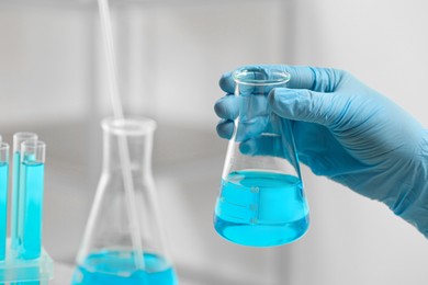 Photo of Scientist holding flask of light blue liquid in laboratory, closeup. Space for text