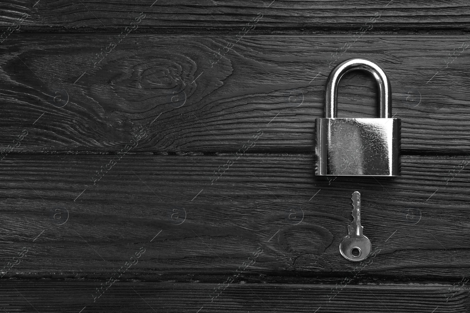 Photo of Modern padlock with key on black wooden table, flat lay. Space for text