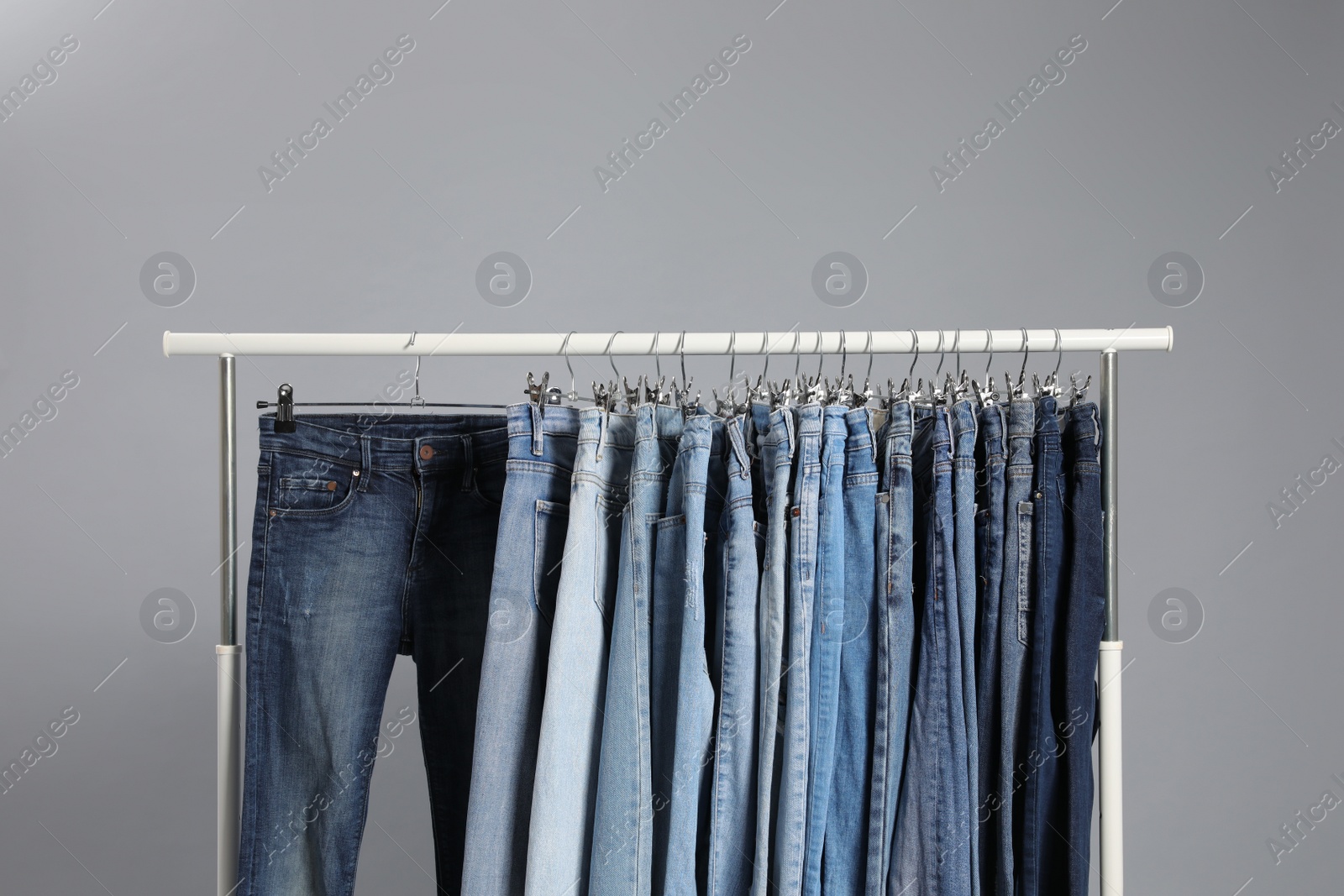 Photo of Rack with different jeans on grey background