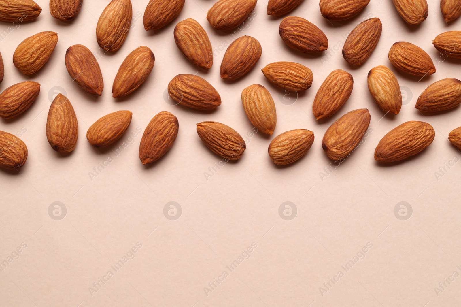 Photo of Delicious raw almonds on beige background, flat lay. Space for text