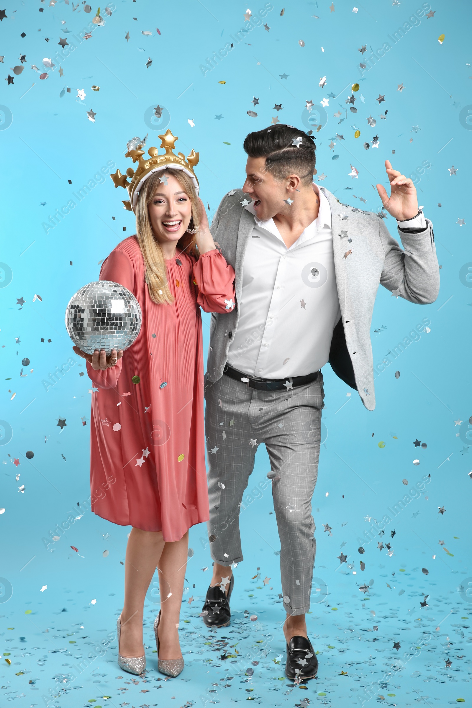 Photo of Happy couple with disco ball and confetti on light blue background