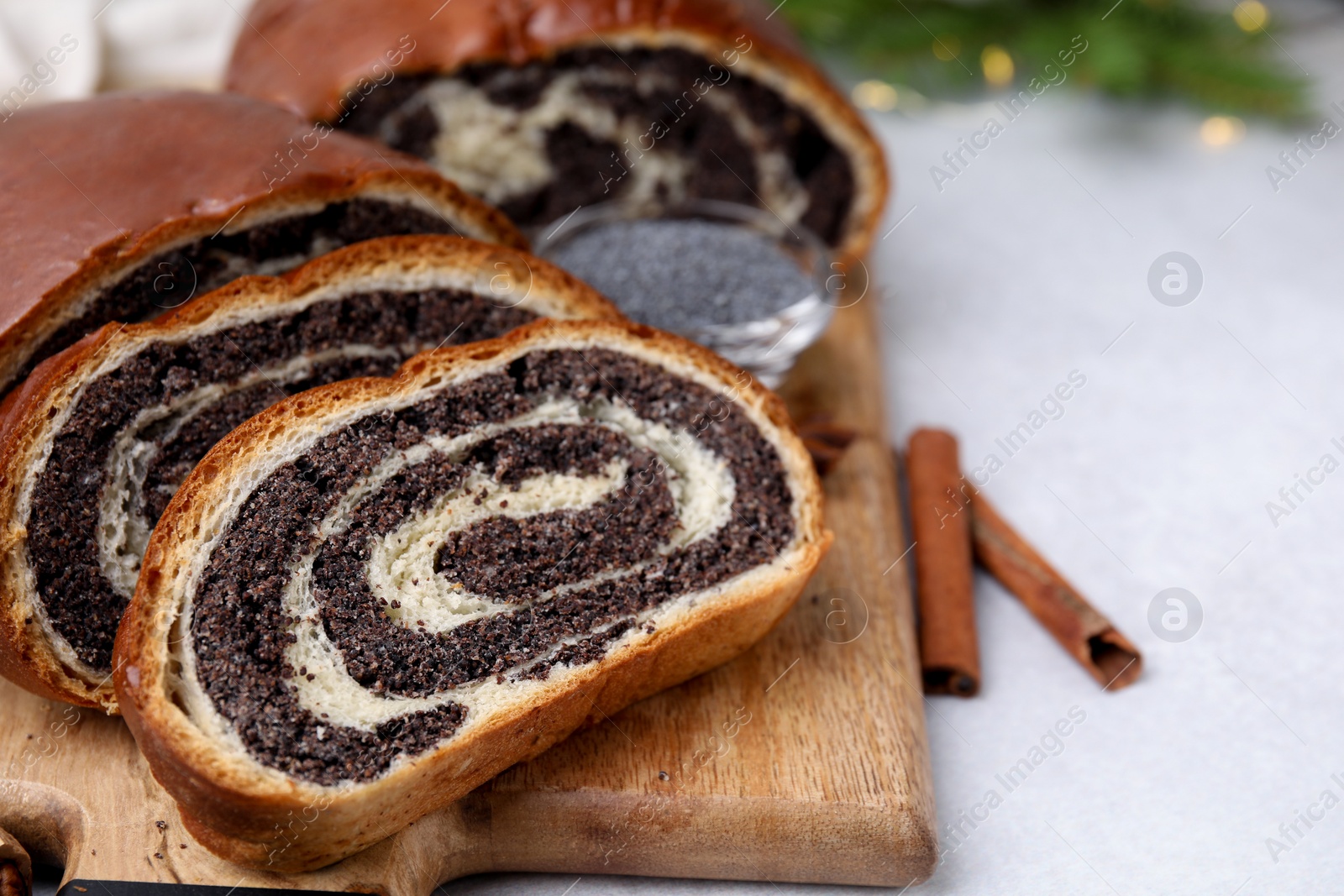 Photo of Cut poppy seed roll and cinnamon sticks on light grey table, closeup with space for text. Tasty cake