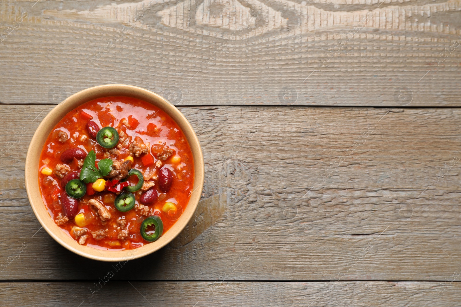 Photo of Bowl with tasty chili con carne on wooden table, top view. Space for text