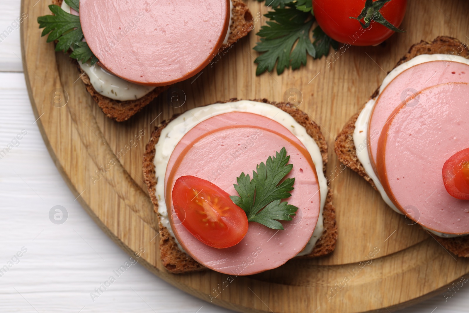 Photo of Delicious sandwiches with boiled sausage, tomato and sauce on white wooden table, top view