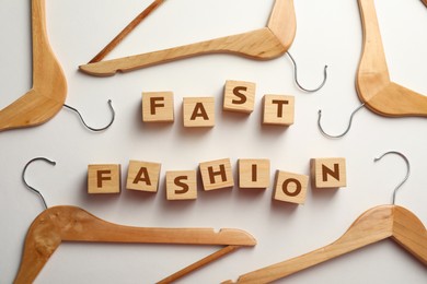 Photo of Wooden cubes with phrase Fast Fashion and hangers on white background, top view