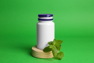 Plastic medicine bottle and leaves on green background. Medicament