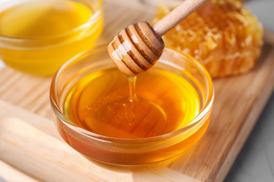 Dripping tasty honey from dipper into bowl on table, closeup