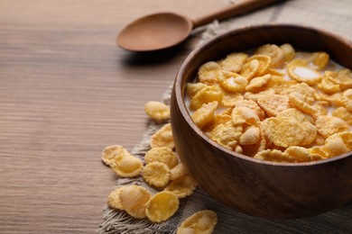 Photo of Tasty cornflakes with milk in bowl served on wooden table, closeup. Space for text