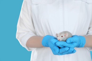 Photo of Scientist holding rat on light blue background, closeup. Animal testing concept