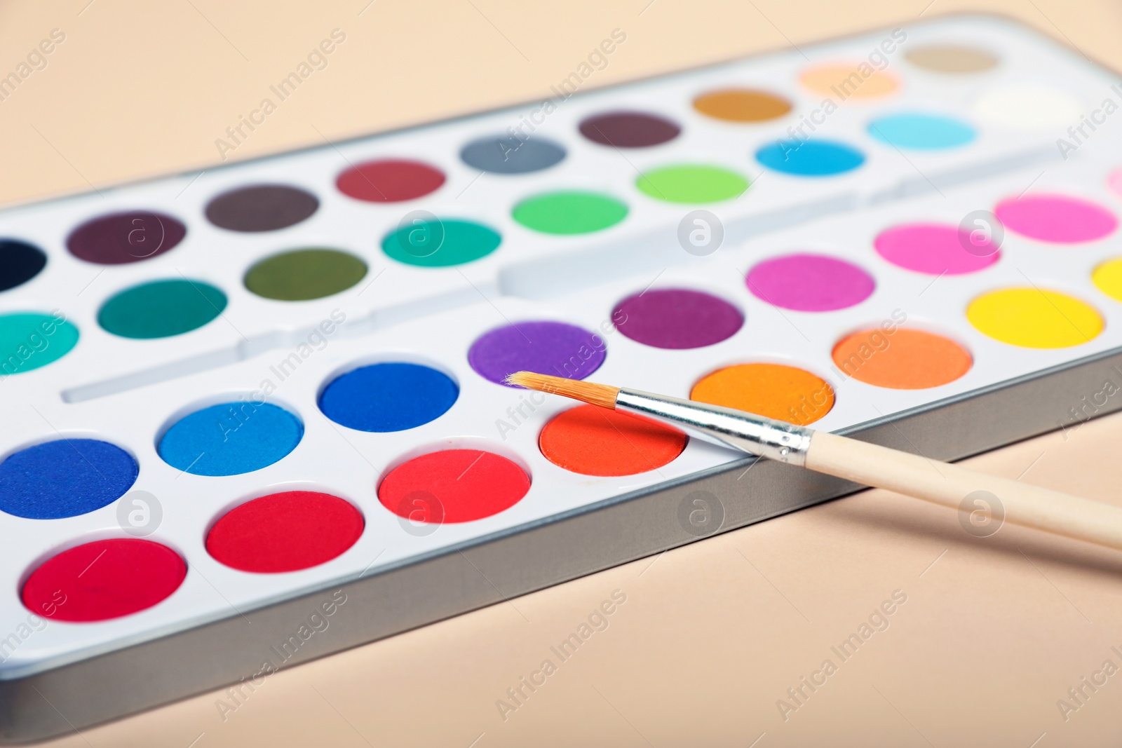 Photo of Watercolor palette with brush on beige background, closeup