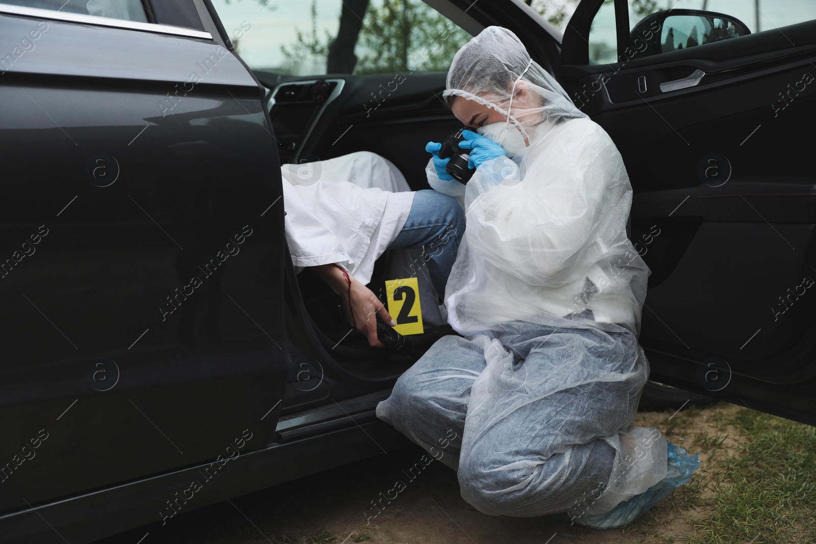 Photo of Criminologist taking photo of evidence at crime scene with dead body in car