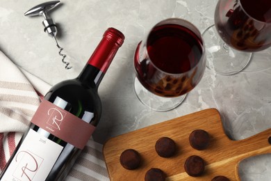 Photo of Glasses and bottle of red wine with chocolate on light marble table, flat lay