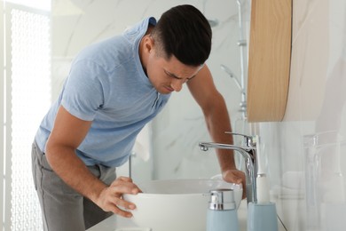 Photo of Man suffering from nausea near sink in bathroom. Food poisoning