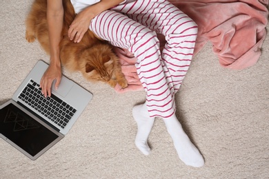 Woman with cute red cat and laptop on light carpet, top view