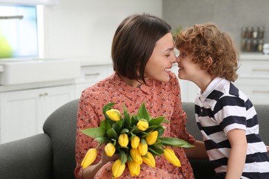 Photo of Little son congratulating his mom with Mother`s day at home. Woman holding bouquet of yellow tulips