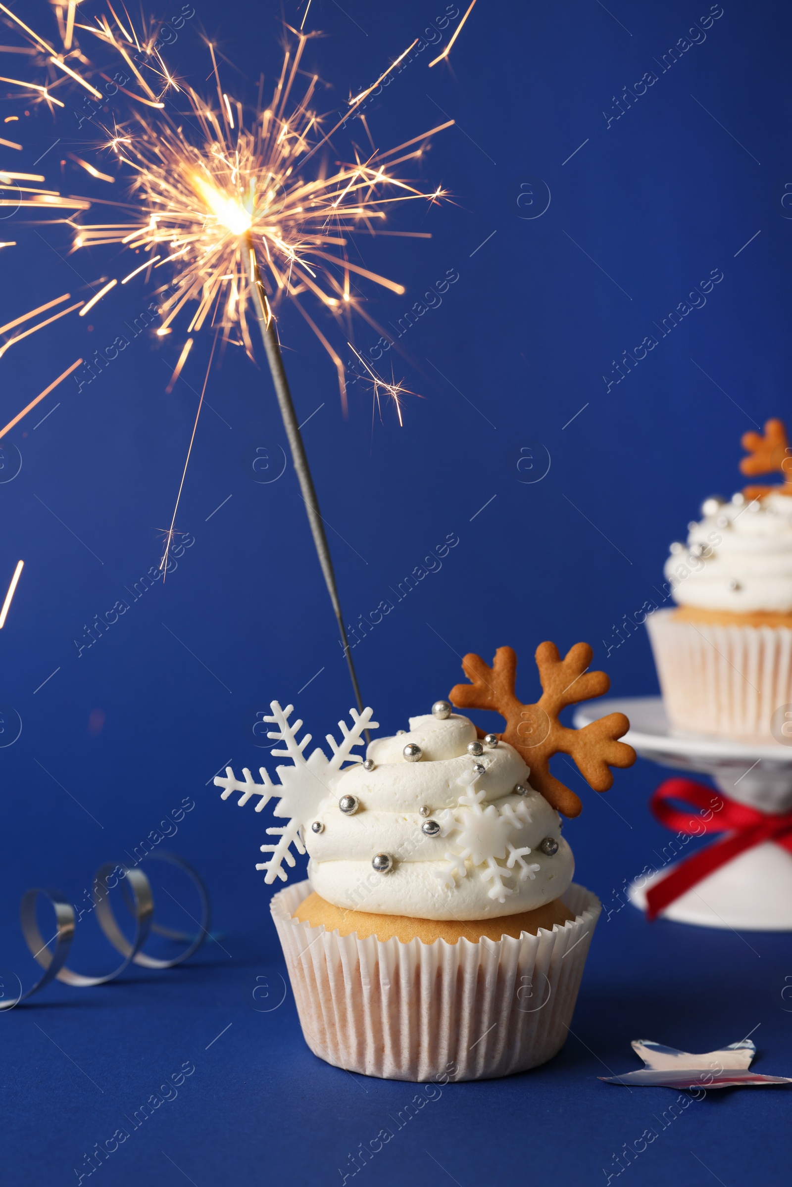 Photo of Tasty Christmas cupcake with snowflakes and burning sparkler on blue background