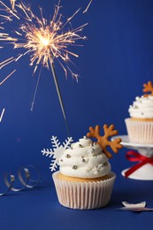 Tasty Christmas cupcake with snowflakes and burning sparkler on blue background