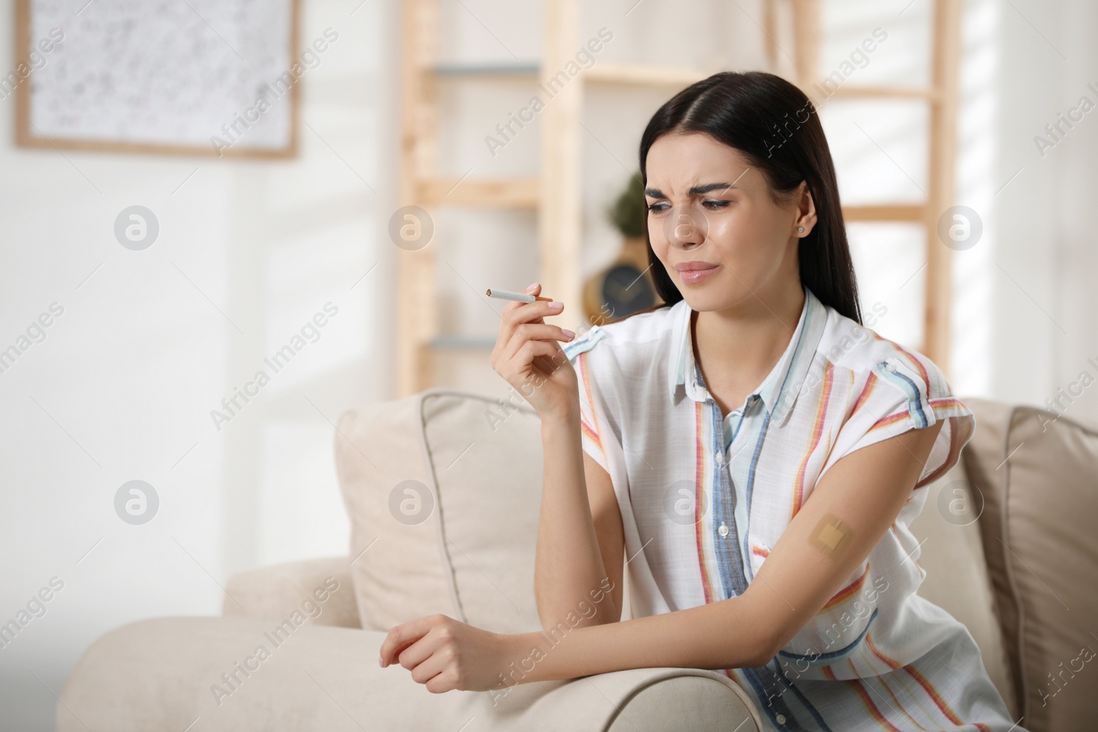 Photo of Emotional young woman with nicotine patch and cigarette at home