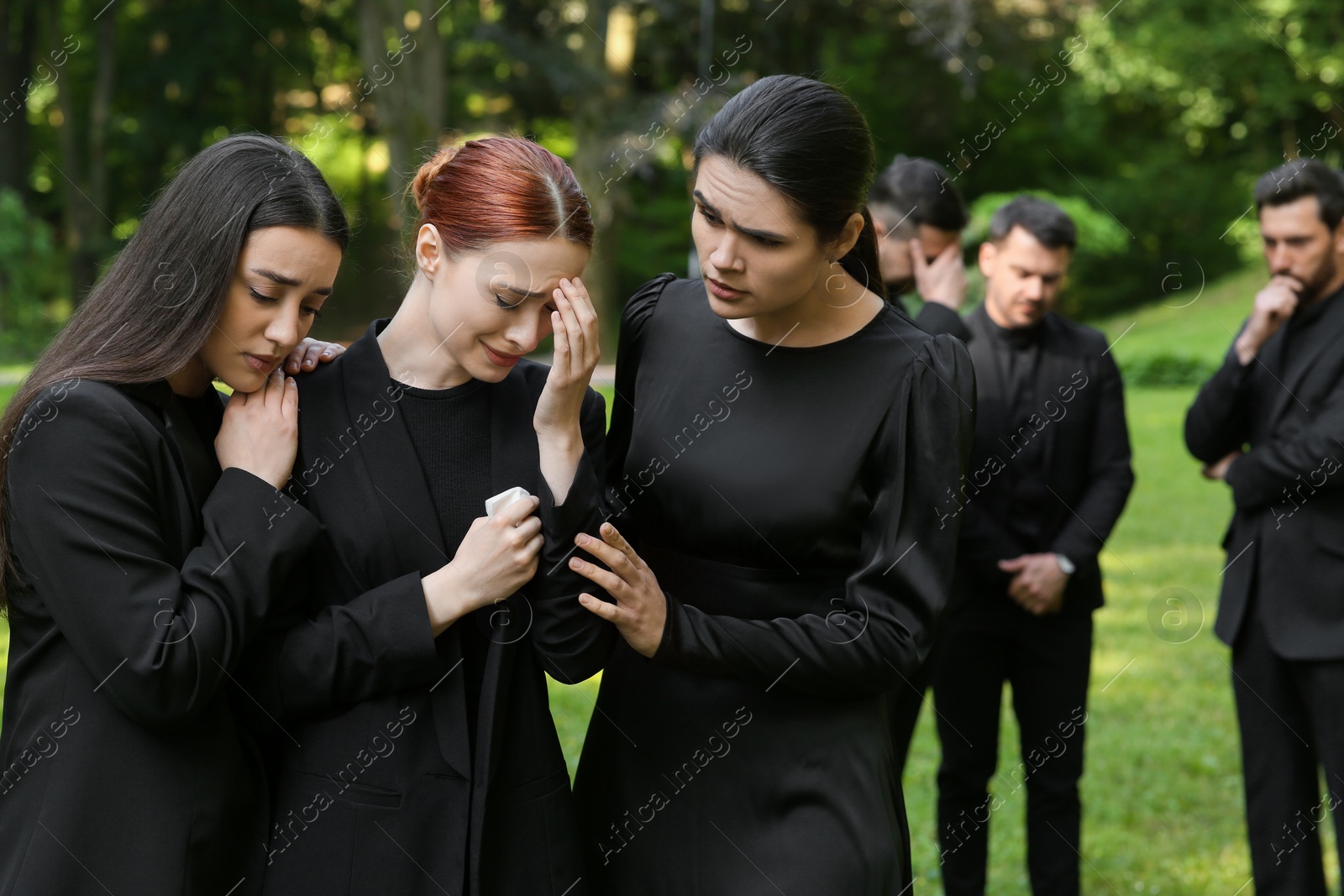 Photo of Sad people in black clothes mourning outdoors. Funeral ceremony