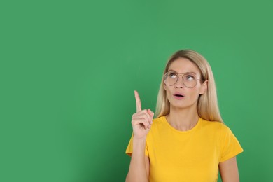 Photo of Happy woman in glasses pointing at something on green background. Space for text