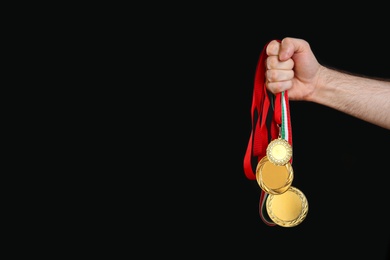 Man holding golden medals on black background, closeup. Space for design
