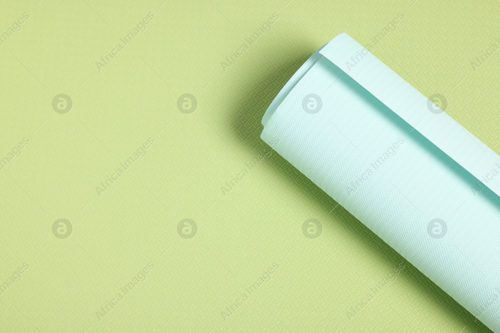 Photo of One light turquoise wallpaper roll on green sample, top view. Space for text