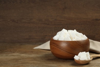 Photo of Bowl and spoon with white sugar cubes on wooden table. Space for text