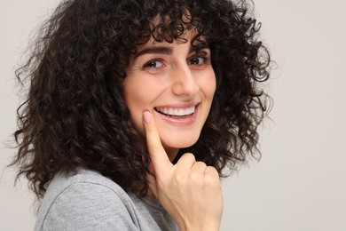 Photo of Young woman showing her teeth with whitening strip on light grey background, space for text