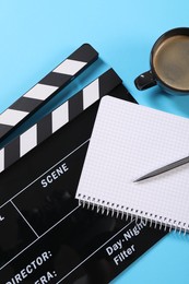 Movie clapper, coffee, notebook and pen on light blue background, flat lay