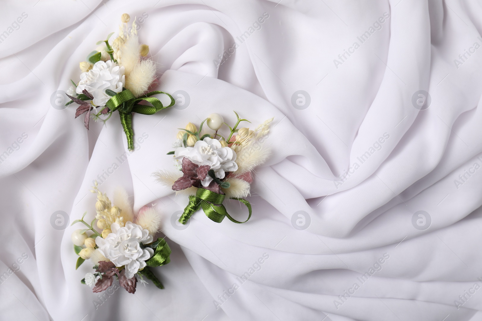 Photo of Stylish boutonnieres on white silk, flat lay. Space for text